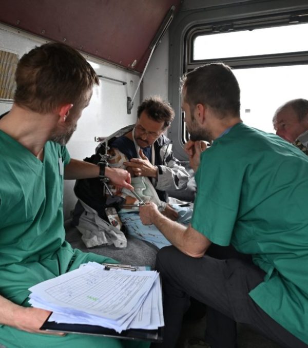 MSF doctors Stig Walravens (2nd R), 33, and Yaroslav (L), 39, care for Oleh, 58, a patient on a medical evacuation train on its way to the western Ukrainian city of Lviv on April 10, 2022. - Doctors Without Borders (MSF), in cooperation with the Ukrainian railways and the Ministry of Health, has just completed a new medical train referral of 48 patients, coming from hospitals close to the frontline in the war-affected east of the country. They include some elderly patients from long-term care facilities, but also a majority of wounded patients. (Photo by Genya SAVILOV / AFP) (Photo by GENYA SAVILOV/AFP via Getty Images)